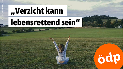 Foto: Blick von hinten auf eine Frau, die auf einer Wiese sitzt und wie erleichtert die Arme in die Höhe wirft. 